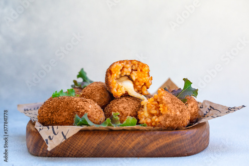 Rice balls stuffed with mozzarella cheese and deep fried on a wooden plate. Light background. photo