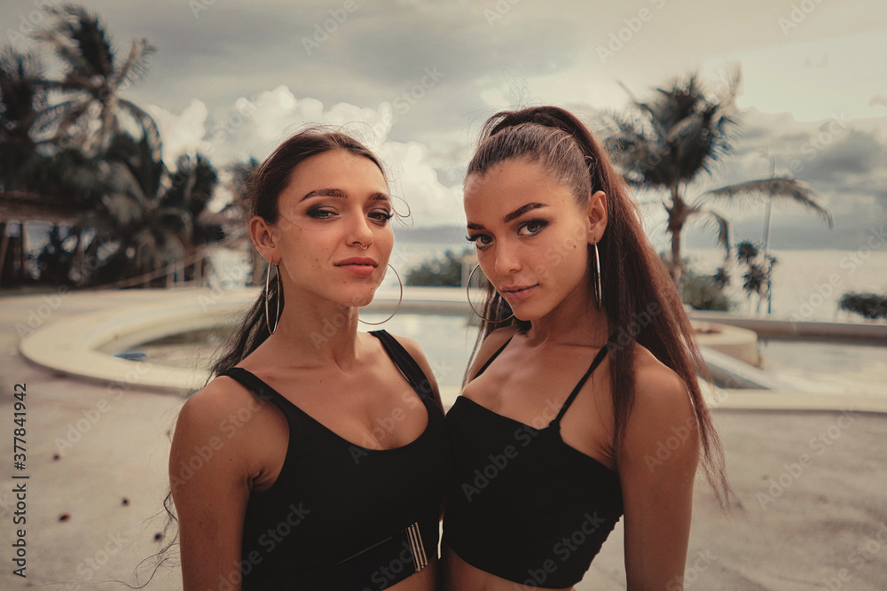 Two beautiful twin sisters Outdoor portrait. beautiful athletic slim bodied twin girls brunettes with long hair