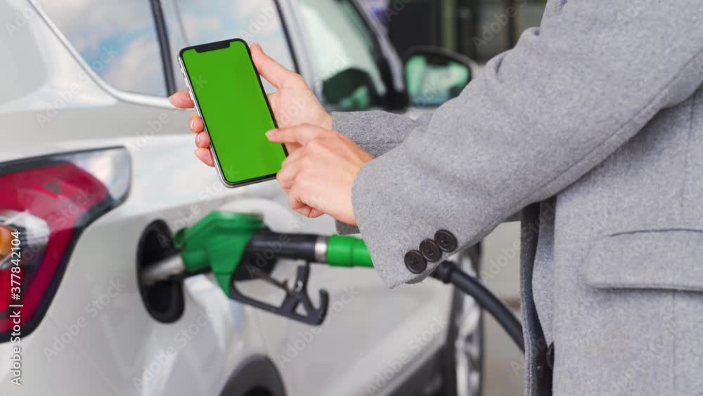Woman uses a mobile application in a smartphone to pay for refueling a car. Smartphone with a green screen. Chroma key Woman uses a mobile application in a smartphone to pay for refueling a car. Smartphone with a green screen. Chroma key