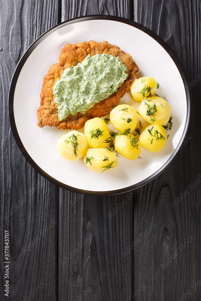 Traditional Frankfurt cuisine schnitzel with boiled new potatoes and green sauce close-up in a plate on the table. Vertical top view from above