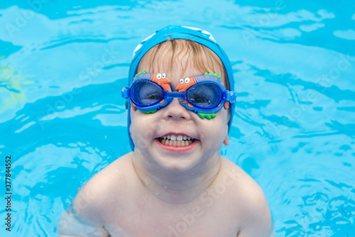portrait of a cheerful child in swimming goggles and a bathing cap in the pool