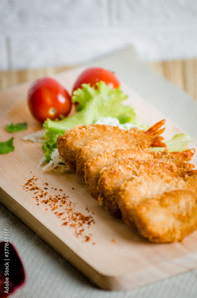 Butterfly ebi furai shrimp served with tomato and lettuce on a wooden chopping board along with ketchup Butterfly ebi furai shrimp served with tomato and lettuce on a wooden chopping board along with ketchup