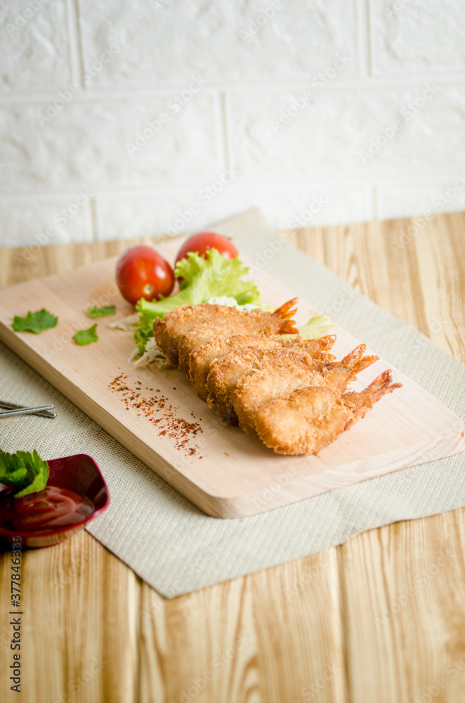 Butterfly ebi furai shrimp served with tomato and lettuce on a wooden chopping board along with ketchup Butterfly ebi furai shrimp served with tomato and lettuce on a wooden chopping board along with ketchup