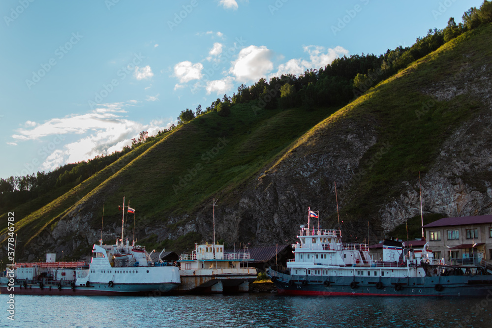 white ships boats in lake baikal near rocks and green mountains with trees in the light of sunset
