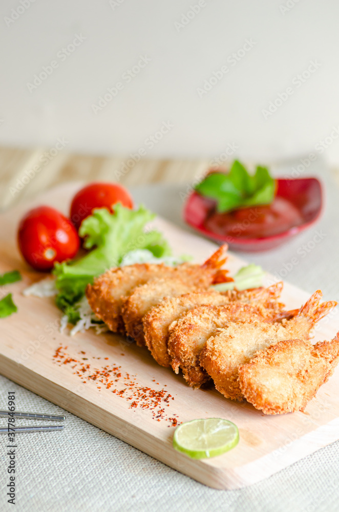 Butterfly ebi furai shrimp served with tomato and lettuce on a wooden chopping board along with ketchup