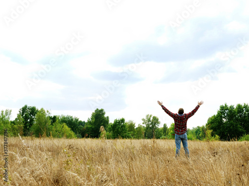 A man in an autumn field stretches out his hands to the sky.