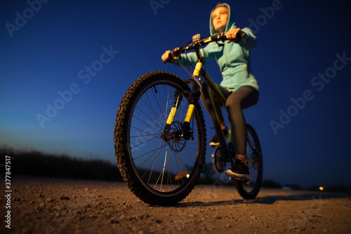 Fototapeta Naklejka Na Ścianę i Meble -  Young woman cycling on bicycle at countryside road at the night