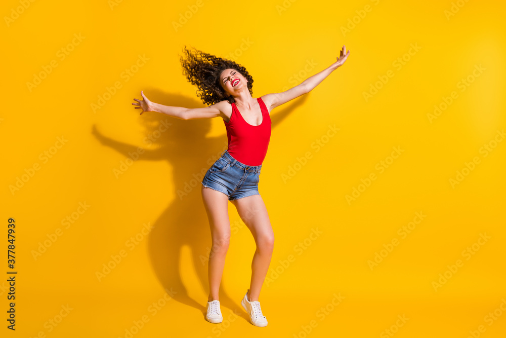 Full length body size photo of funny hipster girl with curly hairdo dancing at party singing wearing jeans mini shorts tank-top isolated on vivid yellow color background