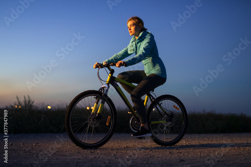Young woman cycling on bicycle at countryside road at the night