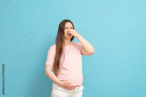 young pregnant woman in pink t-shirt on blue background, toxicosis during pregnancy