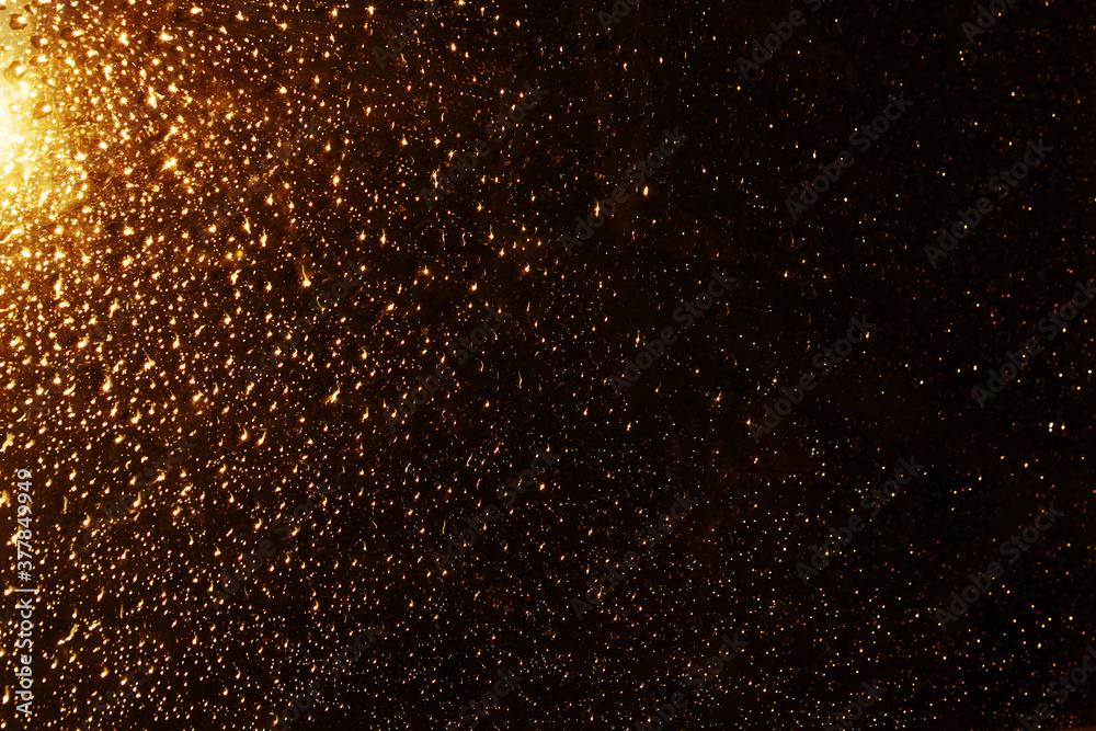 Water drops on a window glass after the rain. Gold sunset or sunrise on dark background.