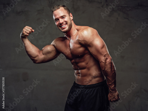Succesful bodybuilder showing his results of trainings and tenacity and posing in studio's special background.