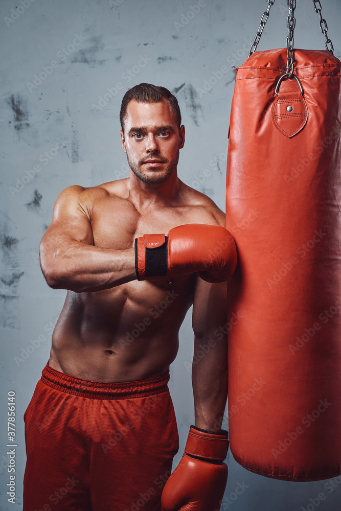 Bodybuilder with huge biceps perfect abs and with protective gloves doing workout with punching bag. Bodybuilder with huge biceps perfect abs and with protective gloves doing workout with punching bag.