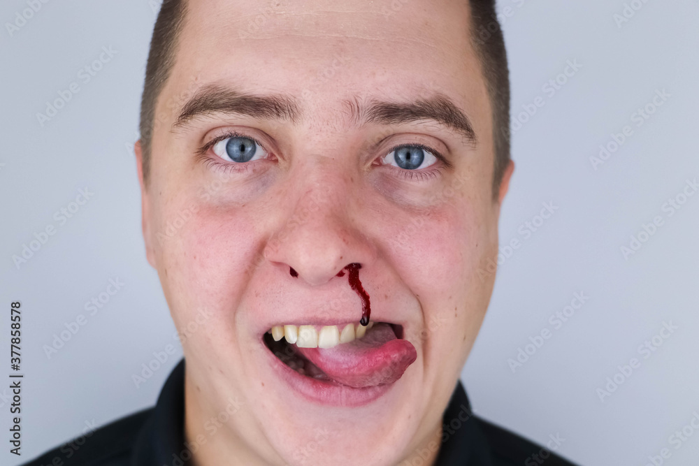 The man is bleeding from his nose, but he smiles. It feels like he likes it. The concept of mazahism, drug addiction, madness and non-standard behavior. The man is bleeding from his nose, but he smiles. It feels like he likes it. The concept of mazahism, drug addiction, madness and non-standard behavior.