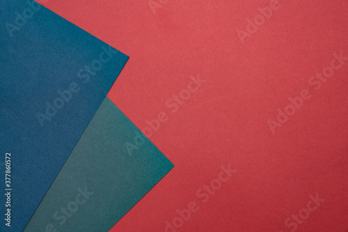 Two sheets of colored paper on a red background. Blue, green, blue. Minimalistic composition. Background for text or design. Empty right side. Top view