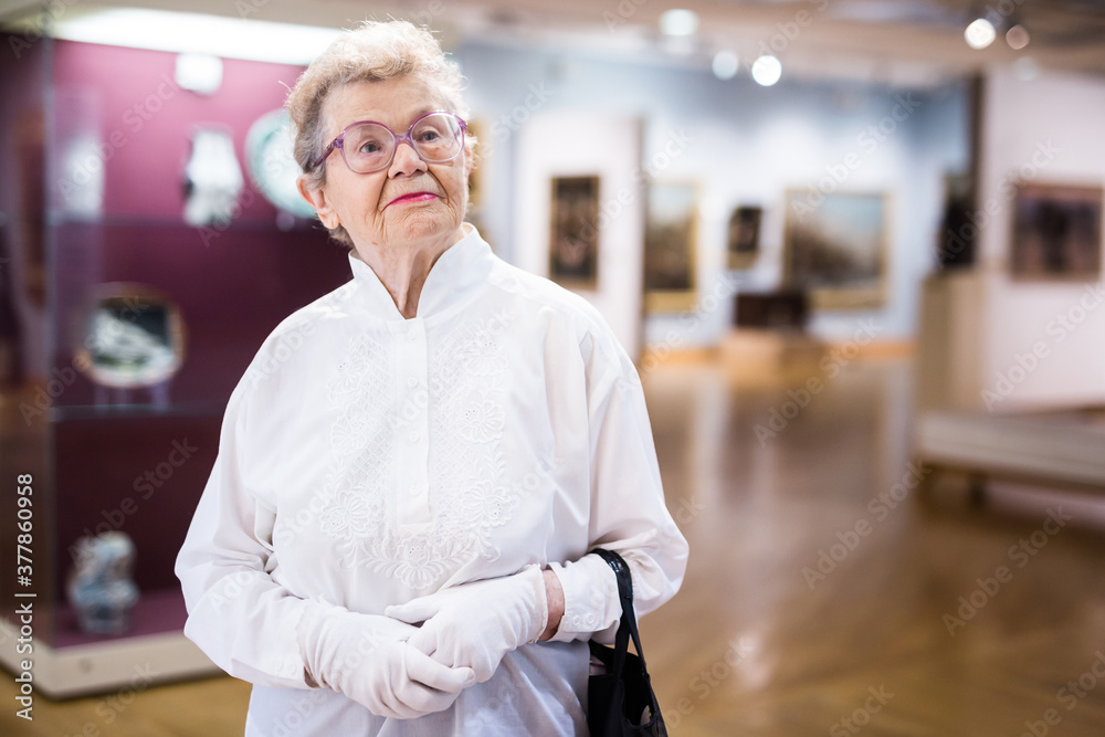 Fototapeta premium mature woman examines paintings in an exhibition in hall of an art museum