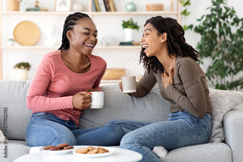 Two african besties laughing while drinking tea together at home photo