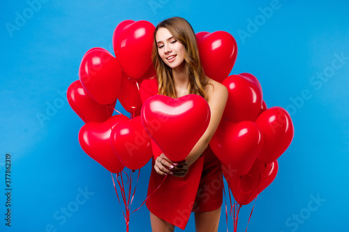 cauasian girl standing around heart shaped balloons on blue background. photo