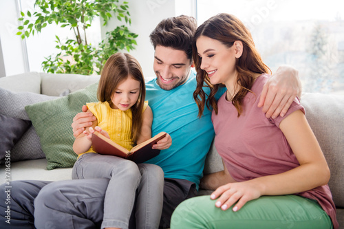 Photo of three people sit cozy couch small id girl read book father mother listen enjoy in house indoors