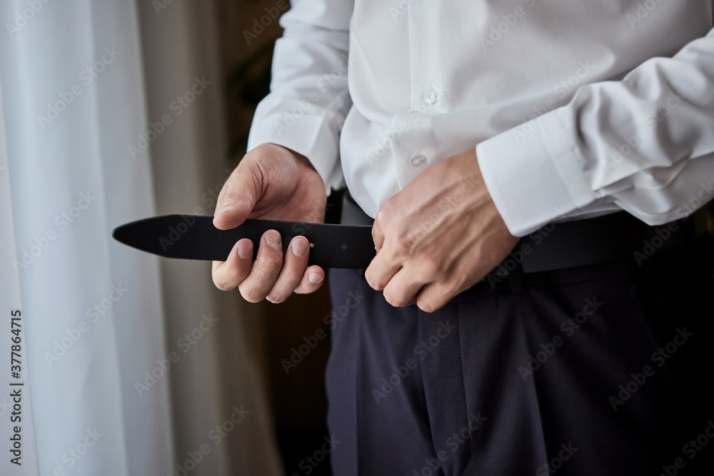 Businessman putting on a belt, fashion and clothing concept,groom getting ready in the morning before ceremony Businessman putting on a belt, fashion and clothing concept,groom getting ready in the morning before ceremony