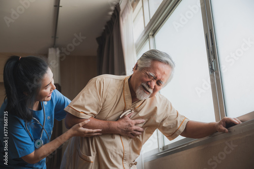 Asian nurse support old male patient with heart and chest pain while standing near the window after treatment at hospital