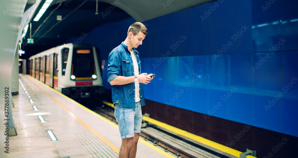 Fototapeta premium Stylish man with smartphone waiting for train