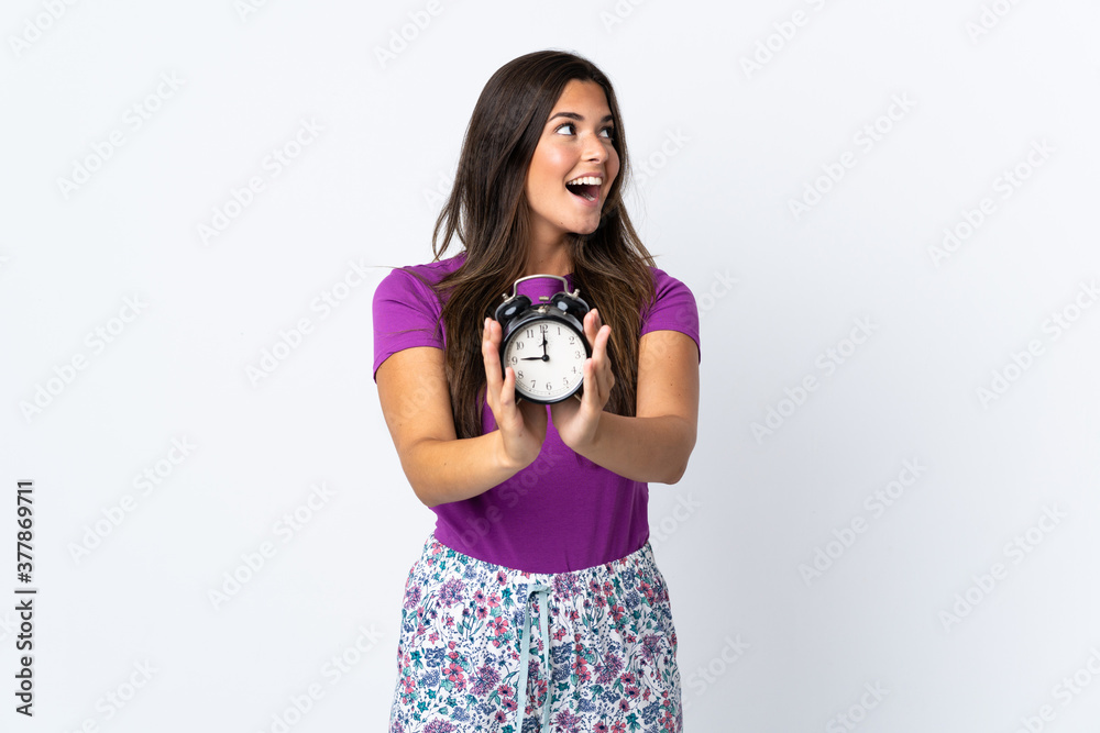 Fototapeta premium Young brazilian girl isolated on white background in pajamas and holding clock