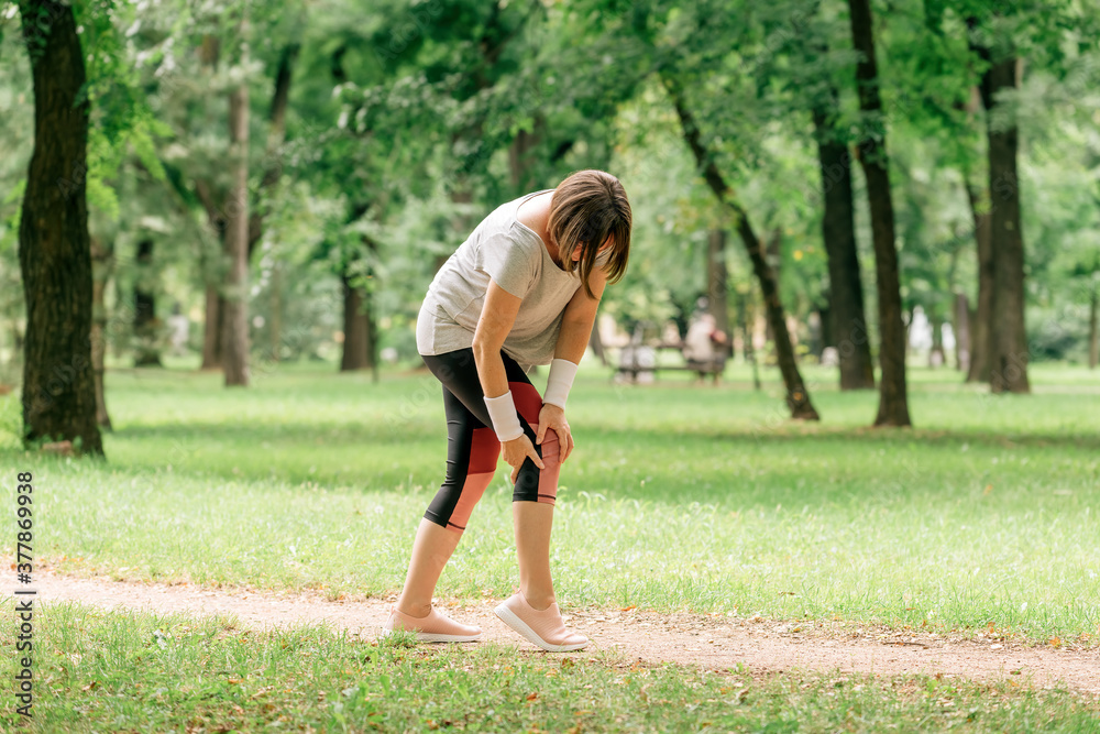 Female jogger with painful knee injury during park jogging activity Female jogger with painful knee injury during park jogging activity