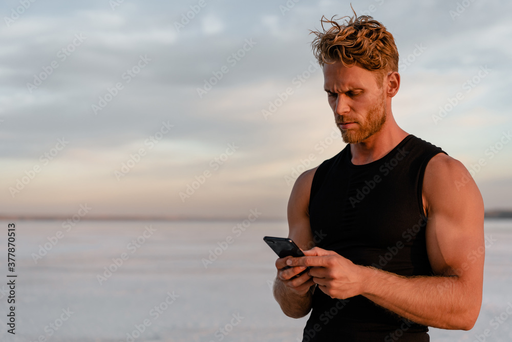 Image of caucasian athletic sportsman using cellphone while working out