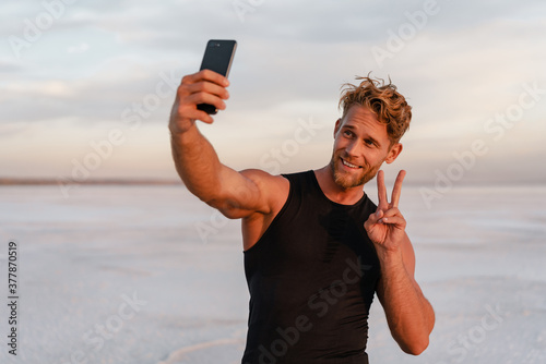 Image of sportsman gesturing peace sign while taking selfie on cellphone photo