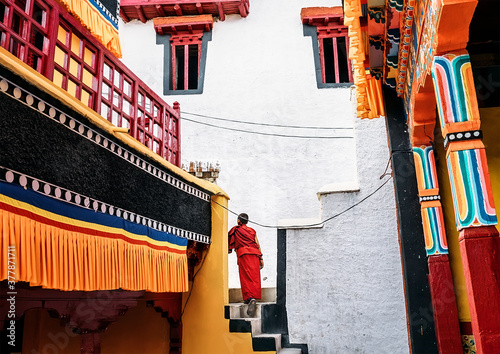 Thiksay Monastery in Thiksey village, India – August 20, 2016: Young monk boy goes by the monastery weared in traditional red kasaya  in Thiksey village, India photo