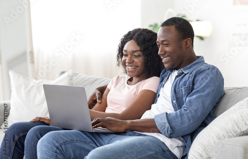 Cheerful black couple using laptop at living room at home