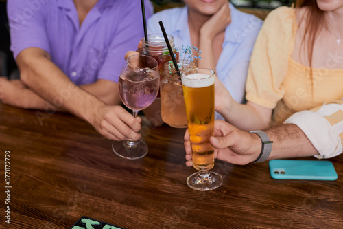 close-up photo of hands clinking glasses wit beer, alcoholic coctails. in the bar