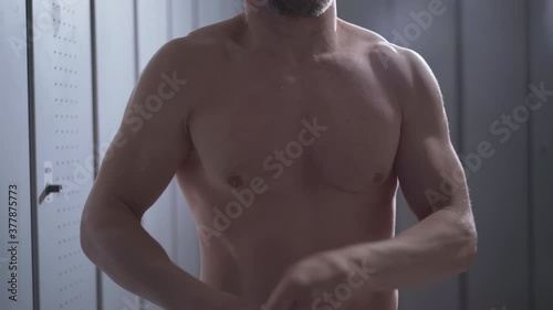 Unrecognizable sportsman taking off blue T-shirt and covering camera with clothes. Athletic Caucasian man changing after workout in gym locker room.