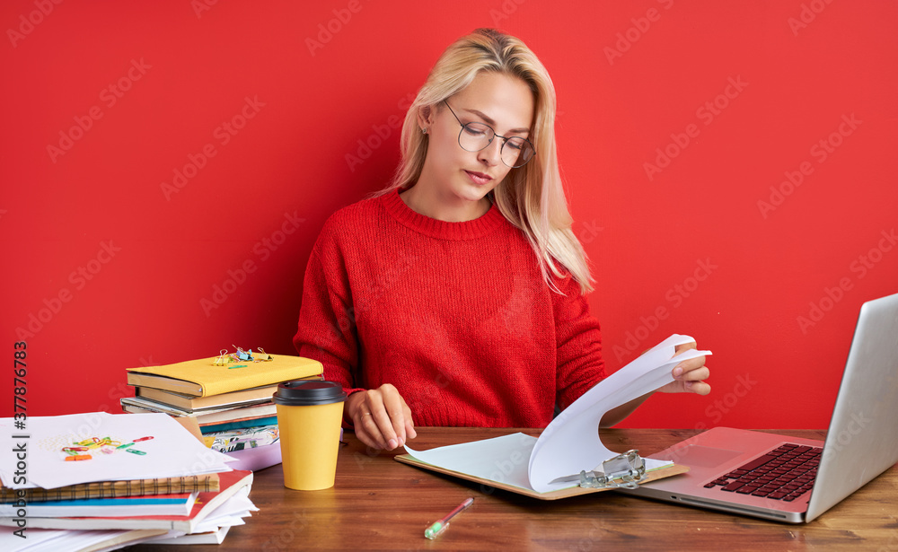young secretary woman is bored at work place, blonde female sit at table with papers, laptop. isolated over red background young secretary woman is bored at work place, blonde female sit at table with papers, laptop. isolated over red background