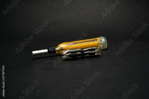 Screwdriver with a universal set of bits, on a dark background.