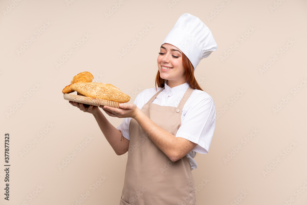 Redhead teenager girl in chef uniform. Female baker holding a table with several breads with happy expression Redhead teenager girl in chef uniform. Female baker holding a table with several breads with happy expression