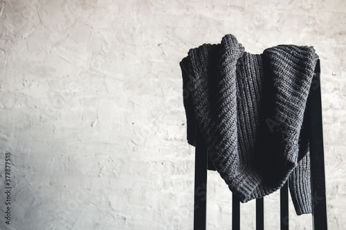 Knitted gray sweater on the back of a white wooden chair