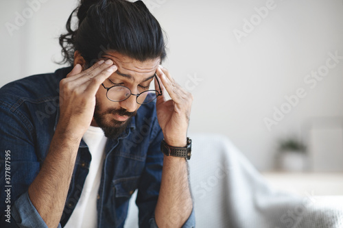 Young indian guy freelancer suffering from headache after hard working day photo