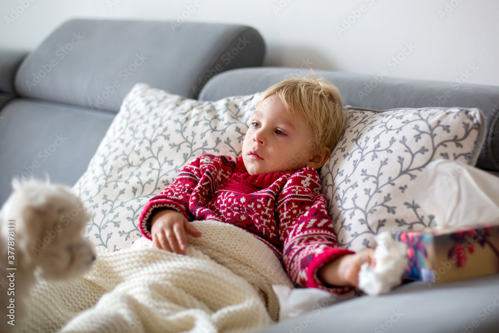 Sick child, toddler boy lying on the couch with his white puppy in living room with fever, resting Sick child, toddler boy lying on the couch with his white puppy in living room with fever, resting