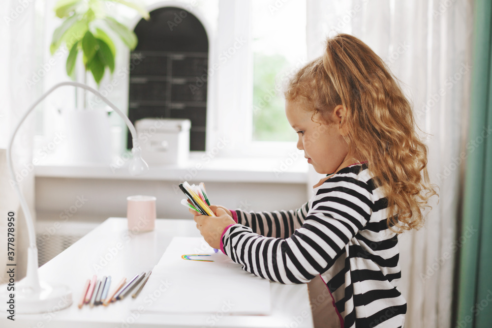A charming girl holds colored pencils in her hands, which she uses to draw a rainbow in an album. Side view, space for text. Home games, homework, home training, social distance A charming girl holds colored pencils in her hands, which she uses to draw a rainbow in an album. Side view, space for text. Home games, homework, home training, social distance