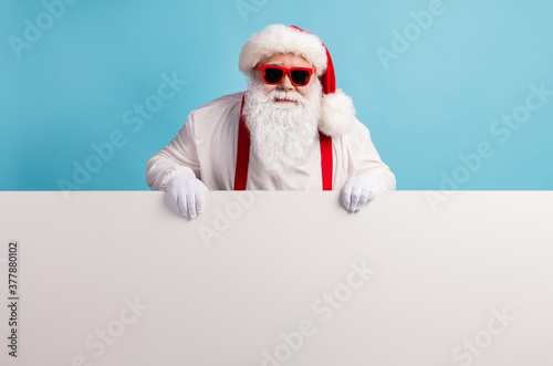 Portrait of his he nice attractive funky cheery confident white-haired Santa holding in hands demonstrating copy space board advert ad isolated over bright vivid shine vibrant blue color background