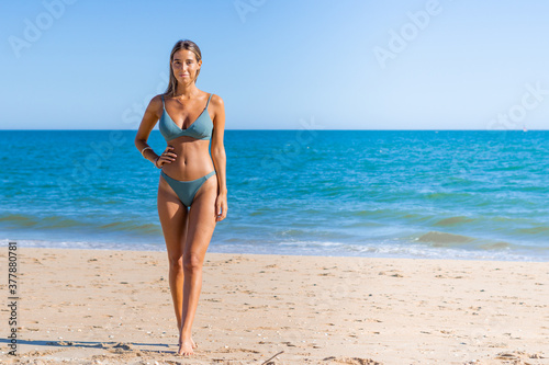 Portrait of young woman in green bikini on tropical beach looking at camera. Beautiful latin girl in swimwear with copy space. Summer vacation and tanning concept.