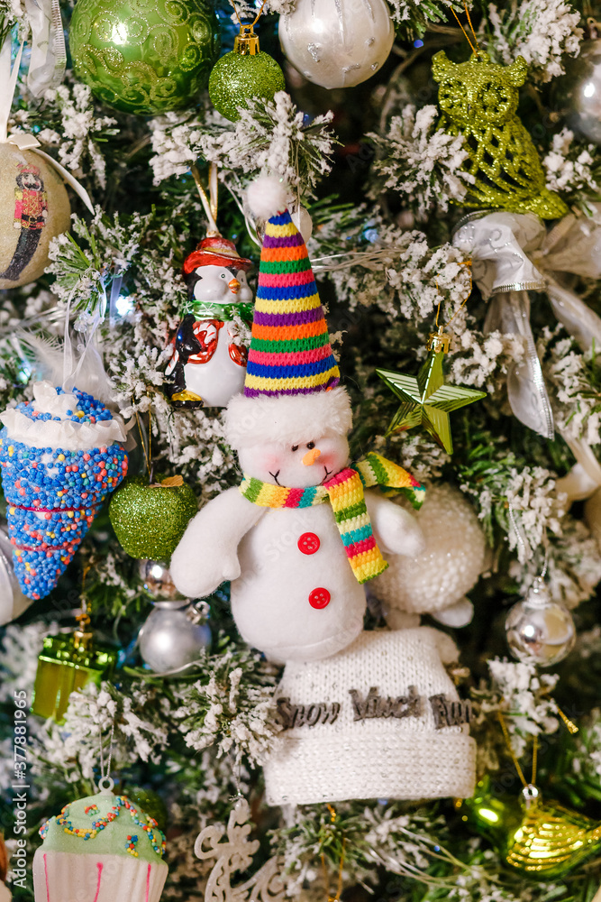 a figure of a cheerful snowman in a striped cap hangs on a Christmas tree.