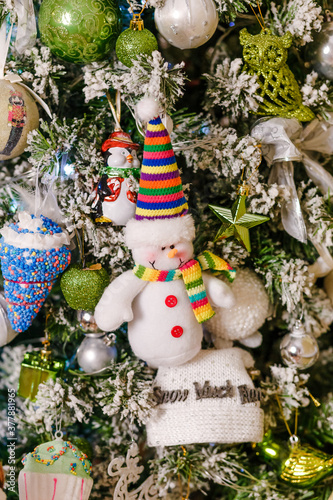a figure of a cheerful snowman in a striped cap hangs on a Christmas tree.