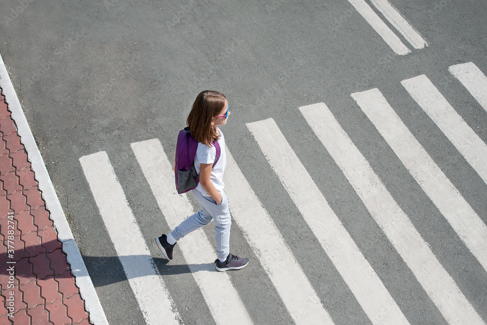 Schoolgirl crossing road on way to school. Zebra traffic walk way in the city. Concept pedestrians passing a crosswalk. Stylish young teen girl walking with backpack. Active child. Top view Schoolgirl crossing road on way to school. Zebra traffic walk way in the city. Concept pedestrians passing a crosswalk. Stylish young teen girl walking with backpack. Active child. Top view