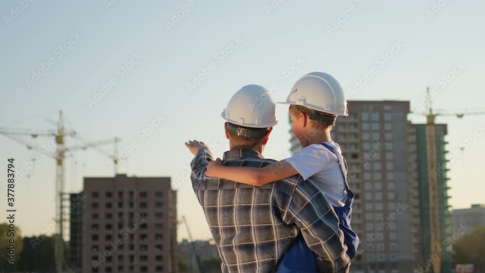 Father and son happy Family concept. Little boy and his dad engineer builder architect with safety helmets, on background new buildings and construction cranes on site. Future profession, 4 K slow-mo