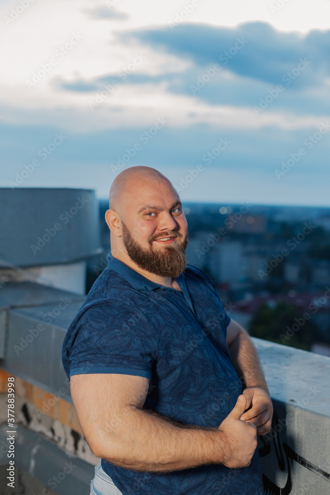 Big bearded bodybuilder on the rooftop in the evening.