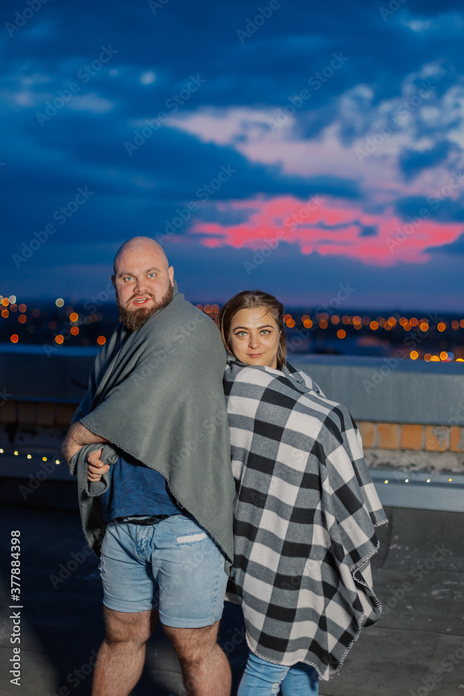Beautiful couple on the roof under a blanket in the evening. Beautiful couple on the roof under a blanket in the evening.