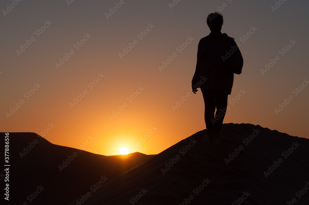 A silhouette of a turist walking on the edge of the Dune 7 during sunset near Walvis Bay in Namibia